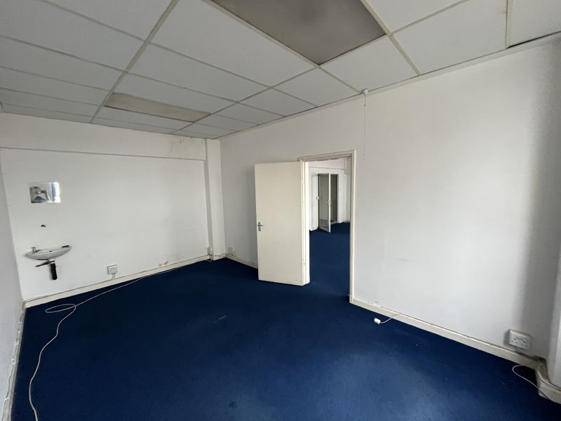 An empty office space featuring a suspended ceiling, blue carpeting, and a wall-mounted basin, offering a blank canvas for professional use.