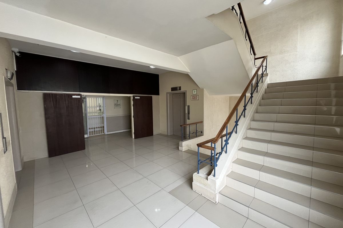 Spacious office building entrance lobby featuring tiled flooring, a central staircase with wooden handrails, and elevator access.