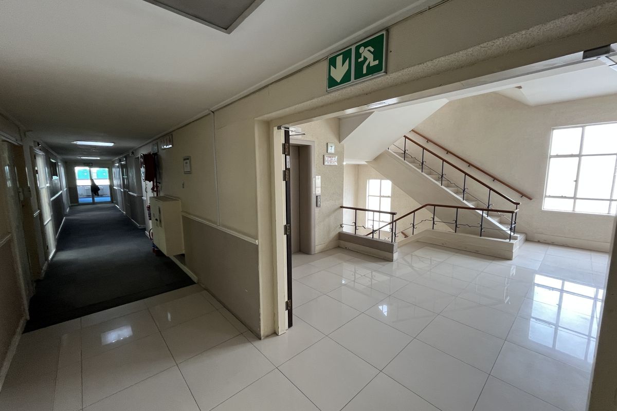 A bright office building hallway featuring tiled flooring, an elevator access point, and a staircase with a decorative wrought iron balustrade.