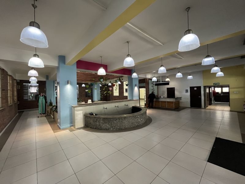 Spacious open-plan commercial interior featuring tiled flooring, multiple pendant lights, a central circular water feature, and a reception counter area.