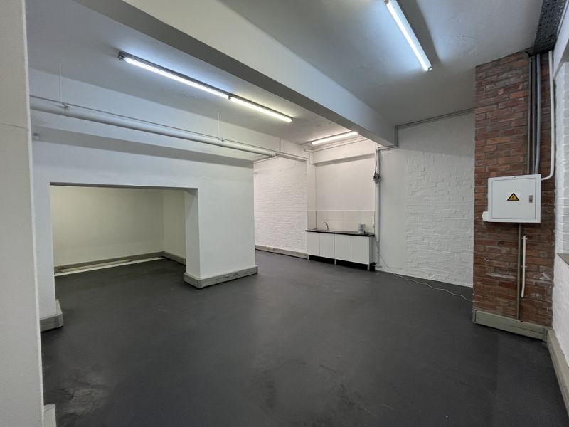 An open-plan utility or commercial space featuring painted brick walls, industrial lighting, concrete flooring, and a compact kitchenette area with a sink.