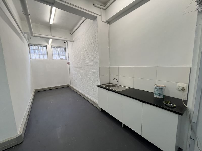 A functional, empty utility or scullery area featuring built-in cabinetry, a stainless steel sink, tiled splashback, and exposed industrial-style ceiling pipes.