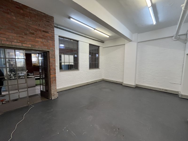 An open-plan office space featuring industrial-style exposed brickwork, steel-framed windows, and painted concrete floors, offering a versatile blank canvas for business operations.