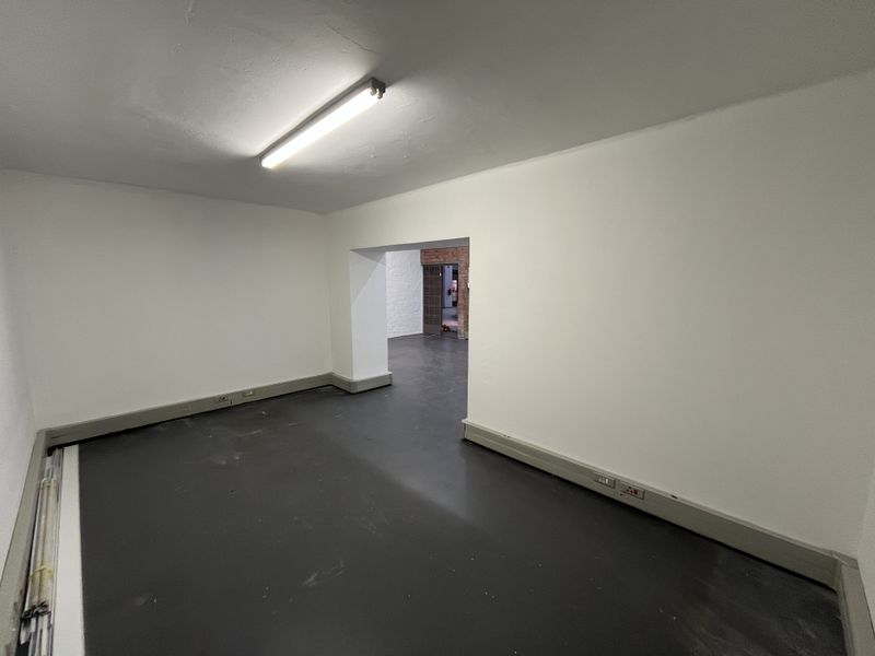 An empty, utilitarian office space featuring dark flooring, white walls, and basic fluorescent lighting, providing a blank canvas for commercial use.