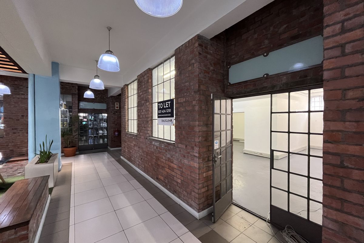 A well-maintained industrial-style hallway featuring exposed brick walls, tiled flooring, and large metal-framed glass doors leading into an open commercial space.