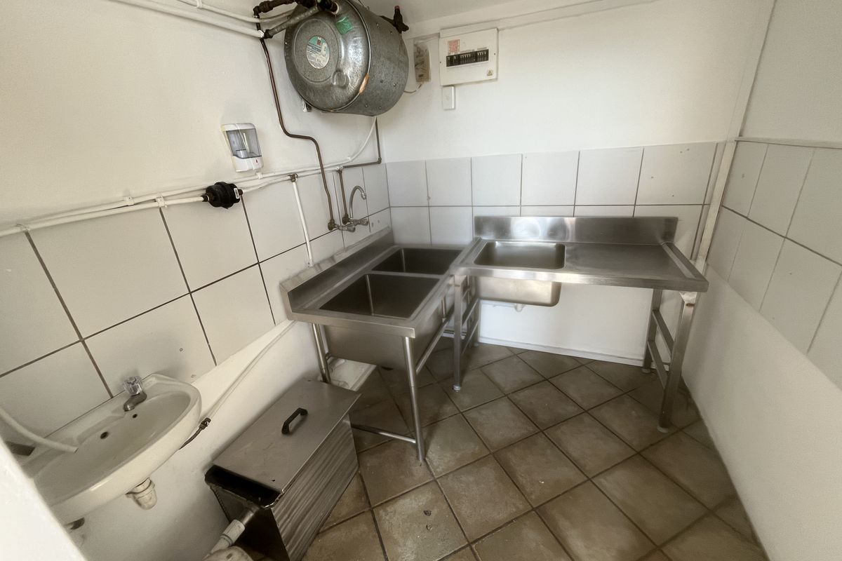 Functional utility or scullery area featuring stainless steel sinks, tiled splashbacks, and exposed utility infrastructure, suitable for commercial or back-of-house operations.