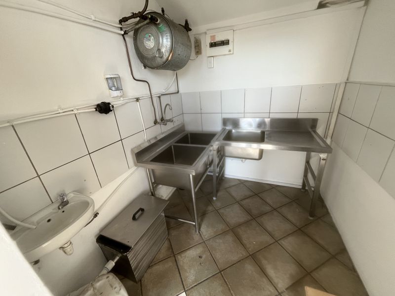 Functional utility or scullery area featuring stainless steel sinks, tiled splashbacks, and exposed utility infrastructure, suitable for commercial or back-of-house operations.