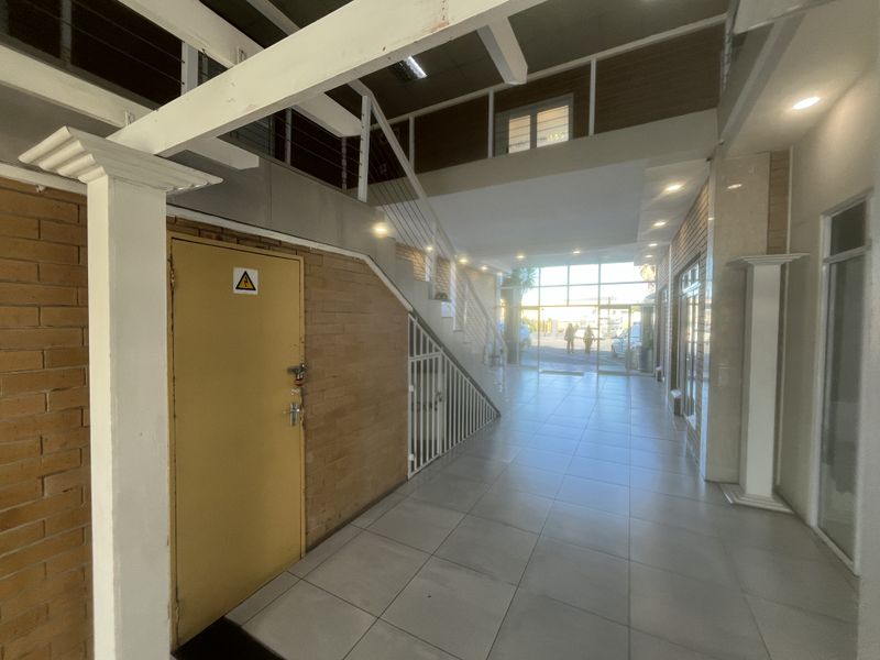 Spacious commercial entrance hall featuring tiled flooring, an exposed brick feature wall, and a staircase leading to an upper mezzanine level.