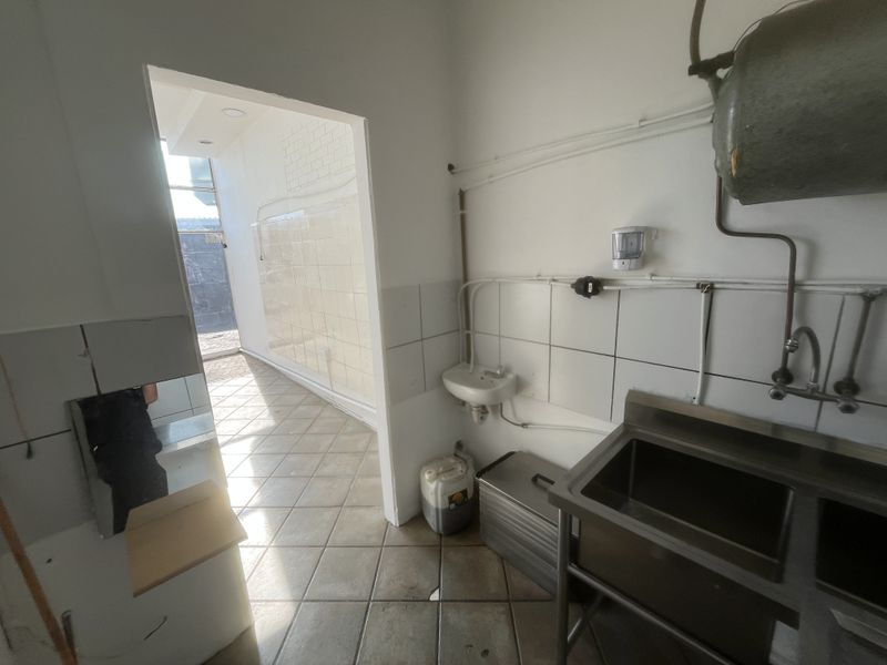 A functional scullery or utility area featuring a stainless steel sink, wall-mounted basin, and tiled finishes, providing a practical space for cleaning and prep.
