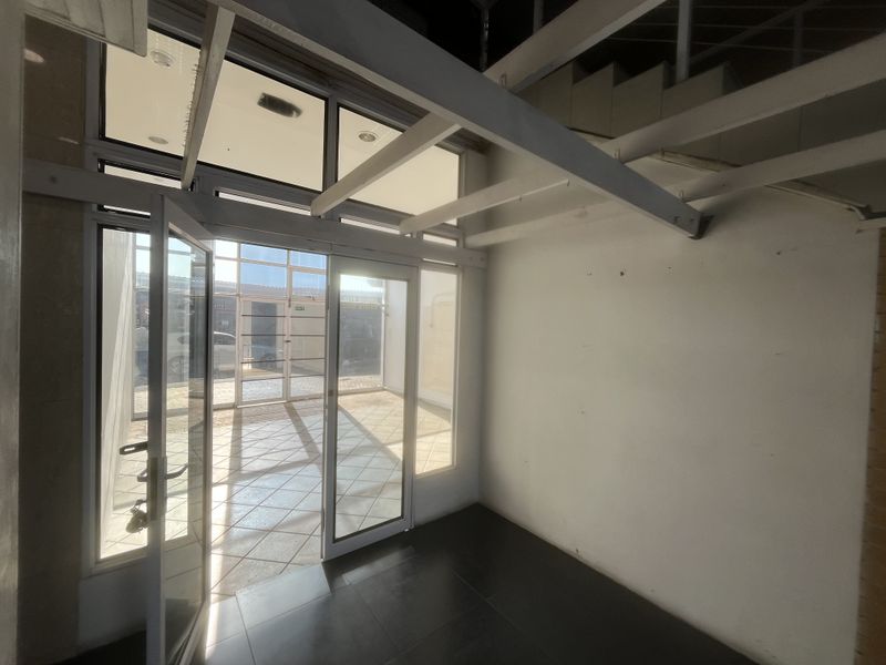 A bright, vacant entrance area featuring glass doors, tiled flooring, and an exposed structural staircase, offering a clean canvas for commercial use.