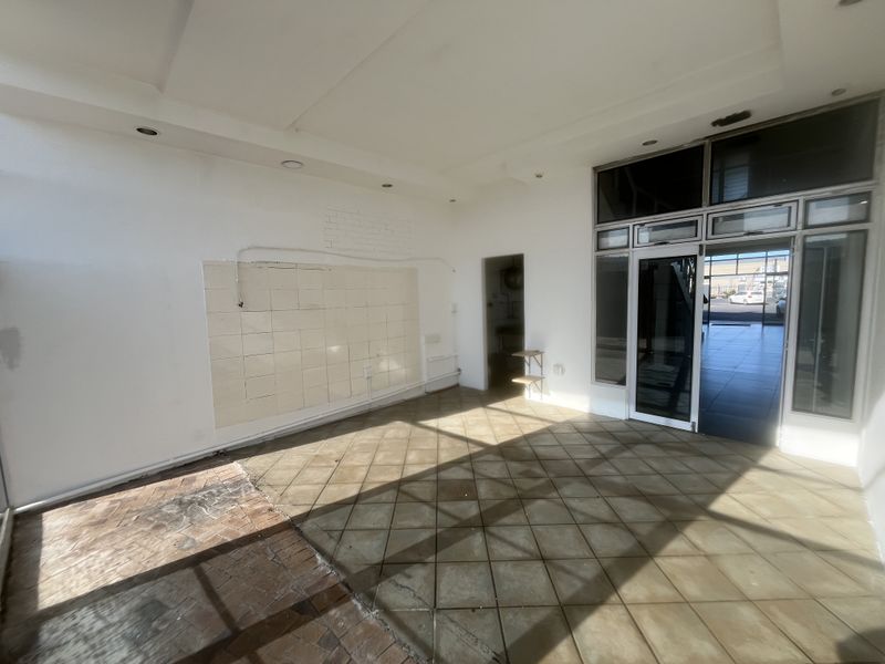 An empty commercial entry space featuring tiled flooring, recessed lighting, and a glass storefront entrance, currently requiring cosmetic updates and repairs.