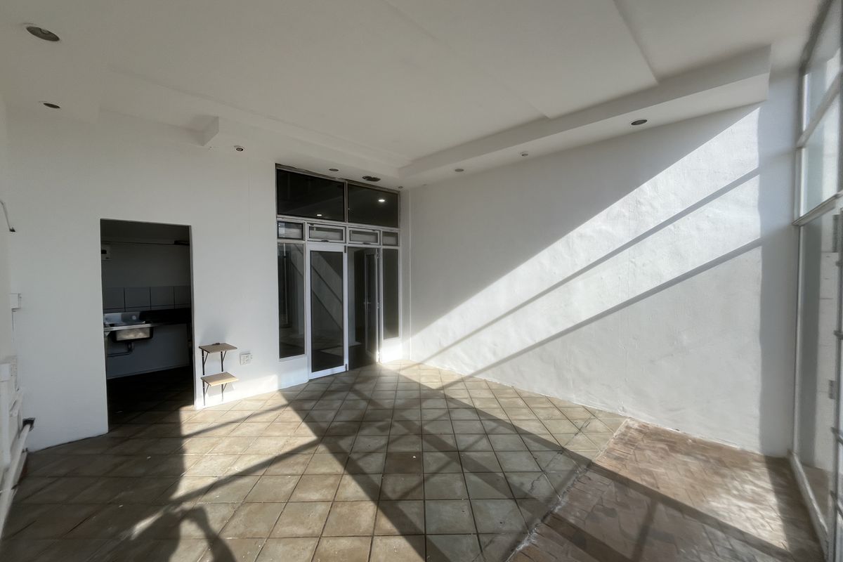 Spacious open-plan area featuring tiled flooring, recessed lighting, and large glass doors, with an adjacent utility space containing a built-in sink.