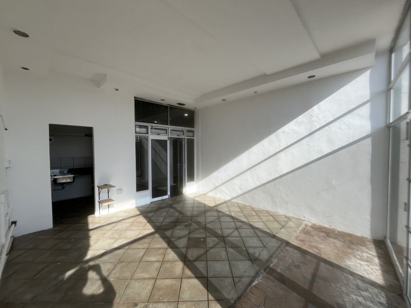 Spacious open-plan area featuring tiled flooring, recessed lighting, and large glass doors, with an adjacent utility space containing a built-in sink.