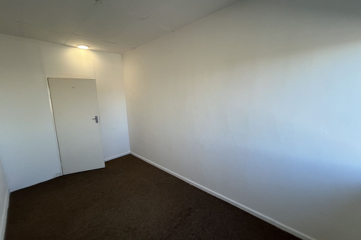 An empty office space featuring brown carpet flooring, a drop ceiling with recessed lighting, and a single internal door.