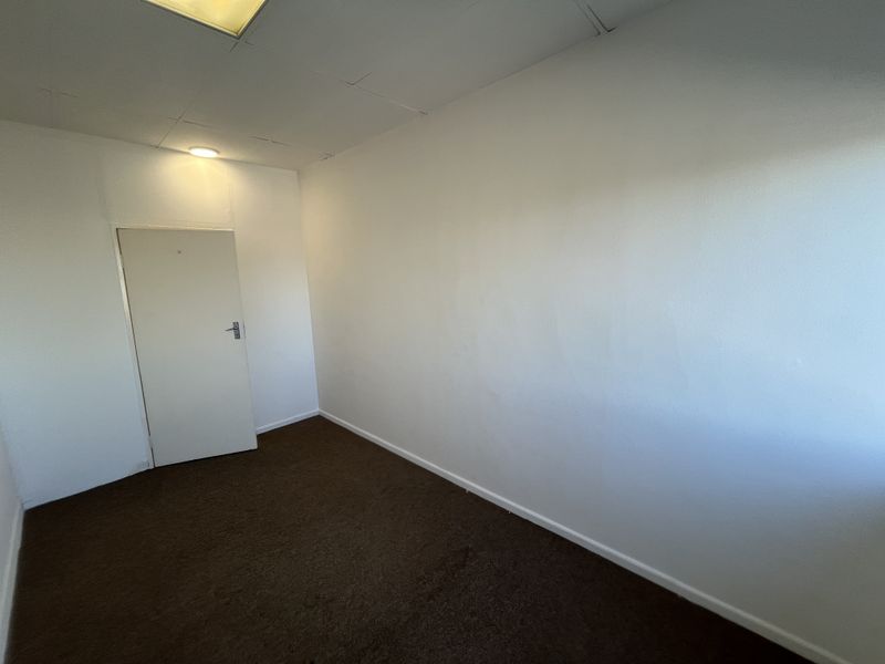 An empty office space featuring brown carpet flooring, a drop ceiling with recessed lighting, and a single internal door.