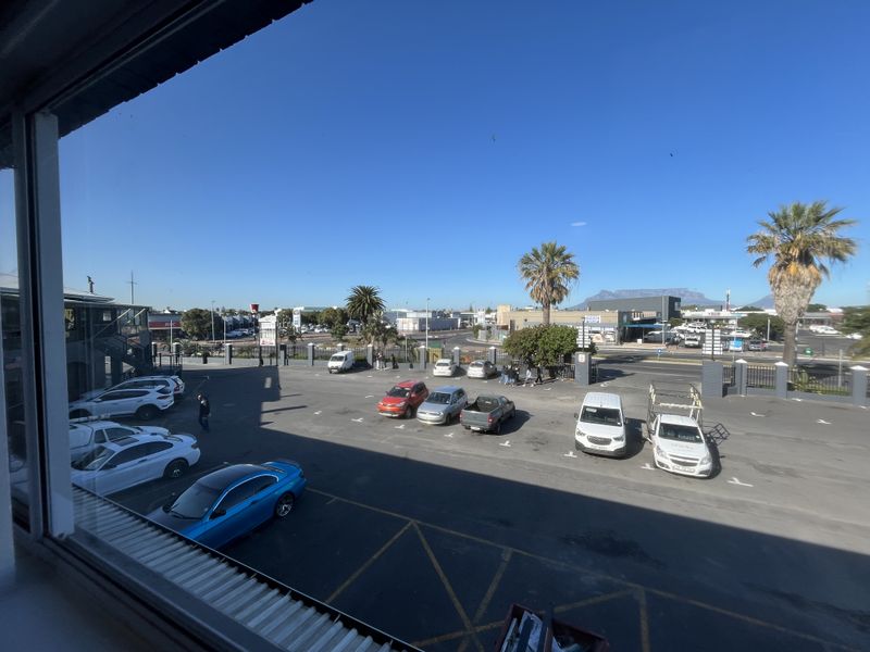 Elevated view from an office window overlooking a paved parking lot, surrounding commercial buildings, and distant mountain scenery.