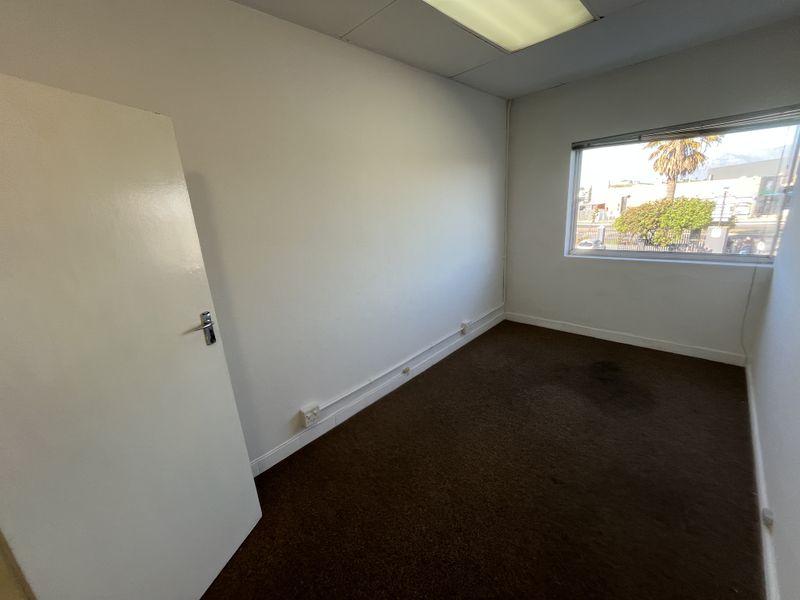 An empty office space featuring a drop ceiling, recessed lighting, and carpet flooring with a window providing natural light.