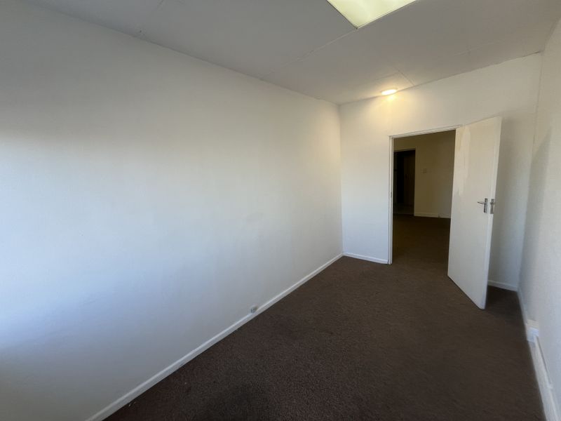 An empty office space featuring brown carpet flooring, white walls, and a drop ceiling with recessed lighting.