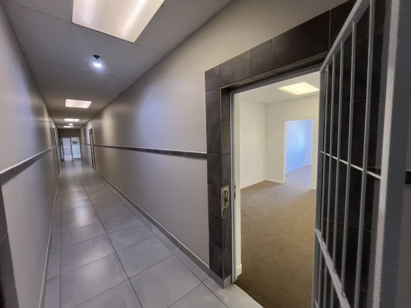 A clean, well-lit office hallway featuring tiled flooring, decorative wall trim, and a security gate leading into an empty office space.