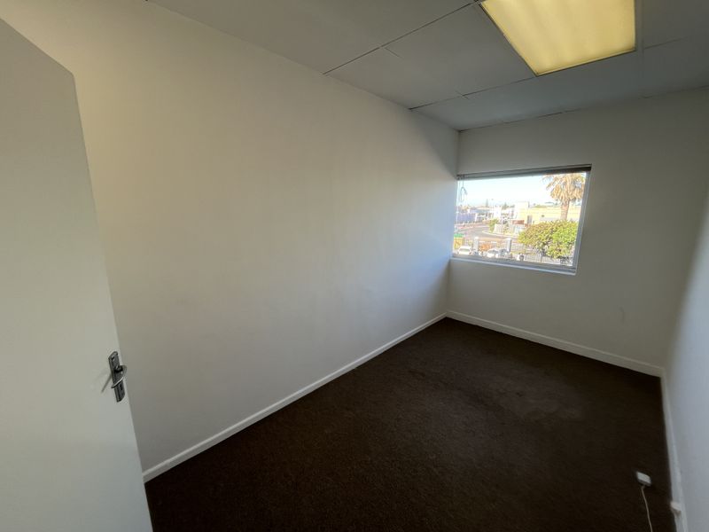 A vacant office space featuring carpeted flooring, a drop ceiling with recessed lighting, and a window providing natural light and exterior views.