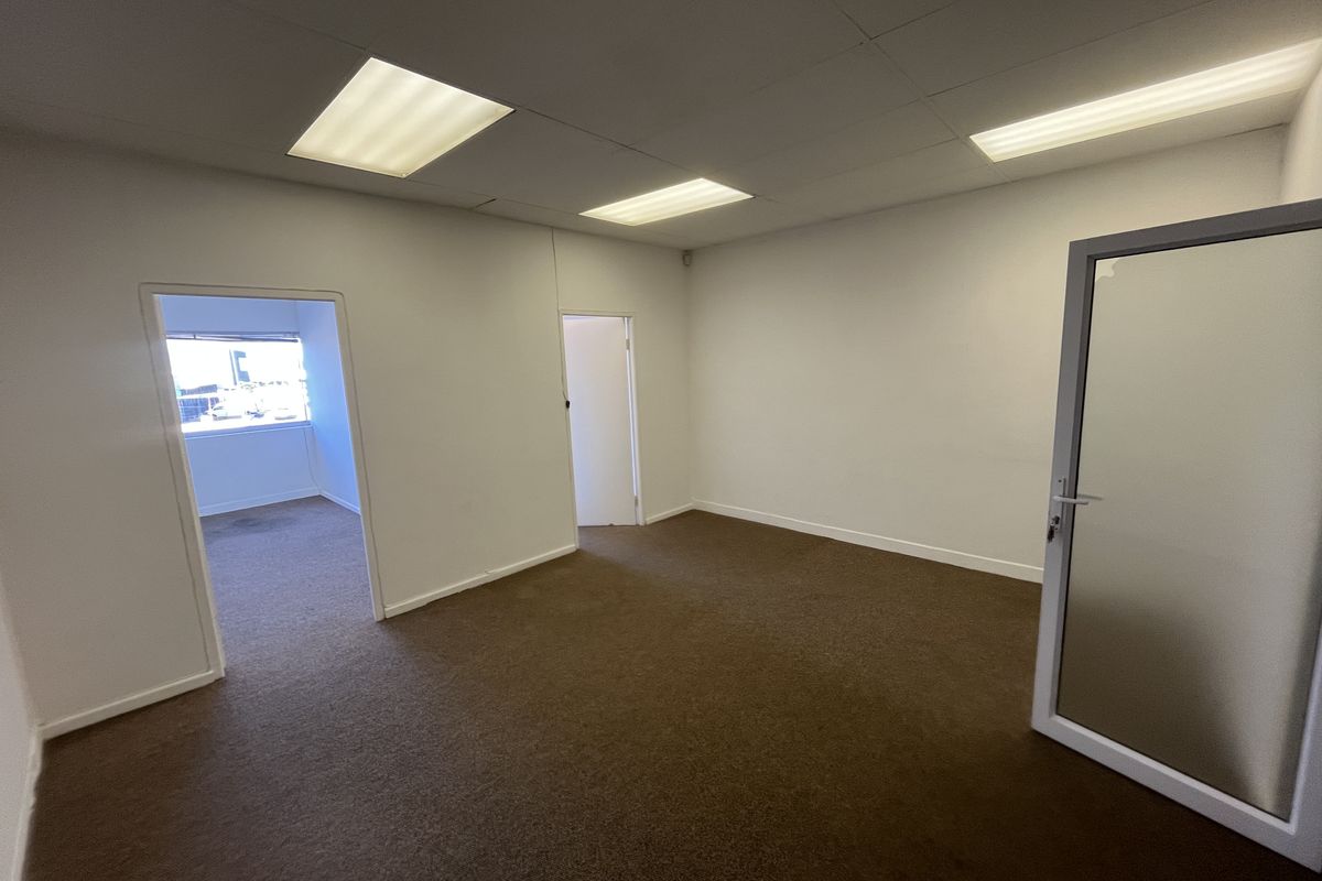 An empty office space featuring carpeted flooring, a suspended ceiling with recessed lighting, and an internal glass door leading to adjacent rooms.