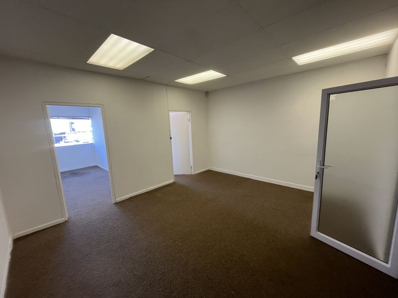 An empty office space featuring carpeted flooring, a suspended ceiling with recessed lighting, and an internal glass door leading to adjacent rooms.