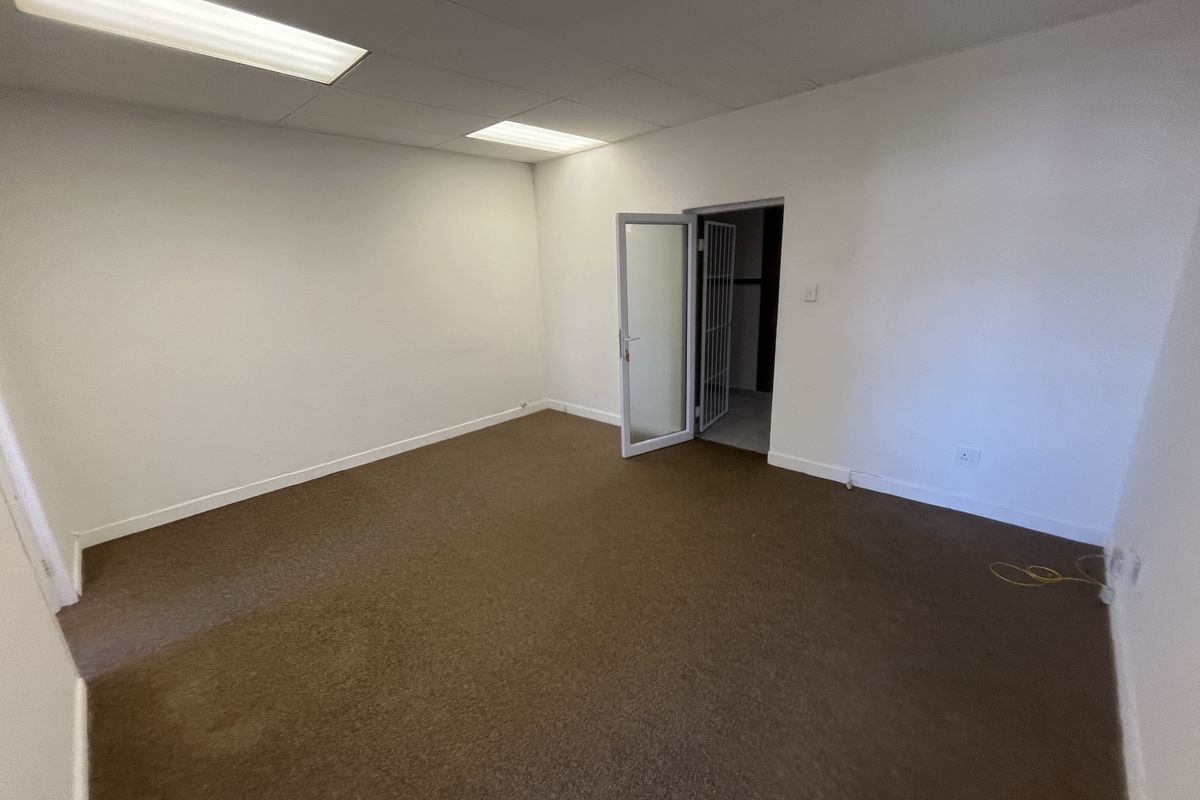 A vacant office space featuring carpeted flooring, a drop ceiling with integrated lighting, and a secure doorway leading to an adjacent area.