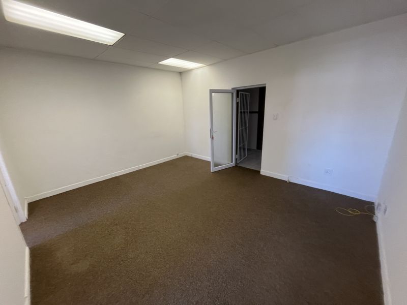A vacant office space featuring carpeted flooring, a drop ceiling with integrated lighting, and a secure doorway leading to an adjacent area.