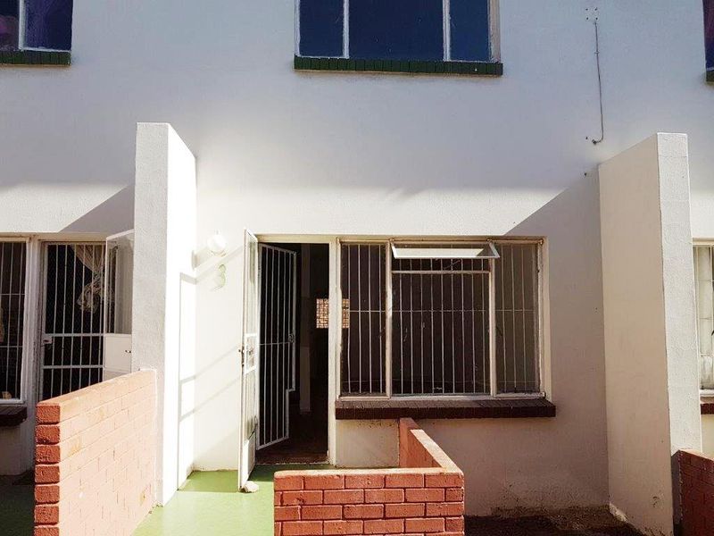 Front entrance of the apartment featuring a security gate, brick boundary wall, and metal-framed windows with security bars.