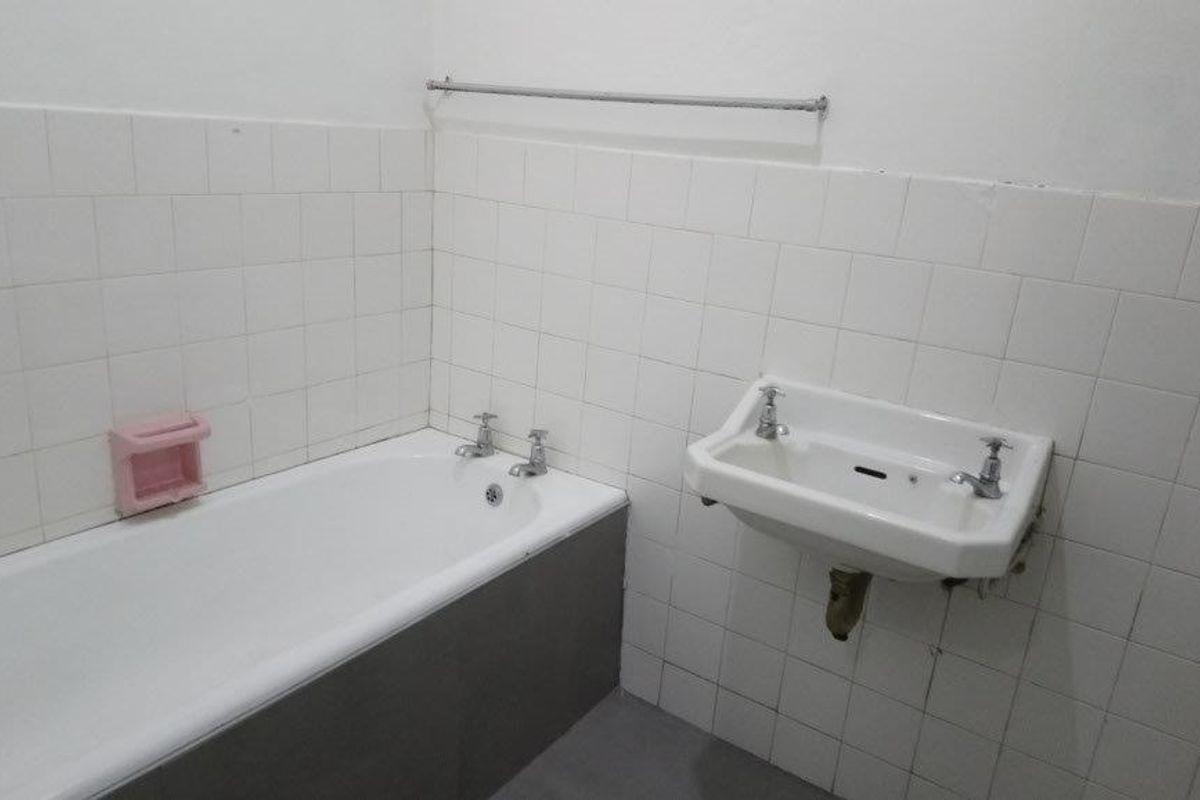 A functional bathroom featuring a standard bathtub and wall-mounted basin with white tiled walls, offering a blank canvas for potential modernization.