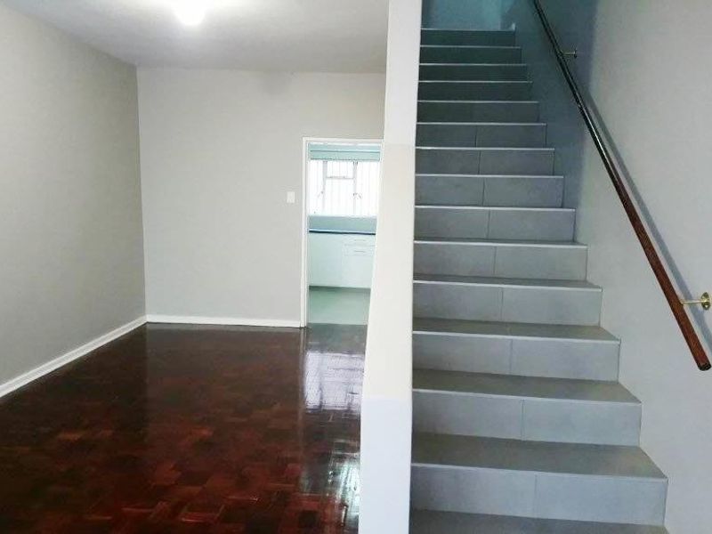 An empty living area featuring polished wooden parquet flooring and a staircase with tiled treads and a wooden handrail.