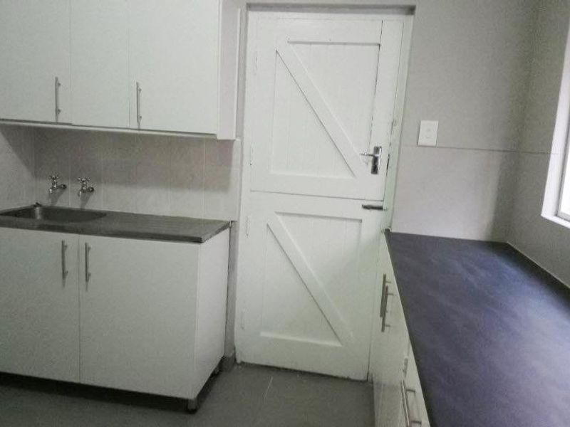 A functional kitchen area featuring white built-in cabinetry, dark laminate countertops, a stainless steel sink, and a classic stable door.
