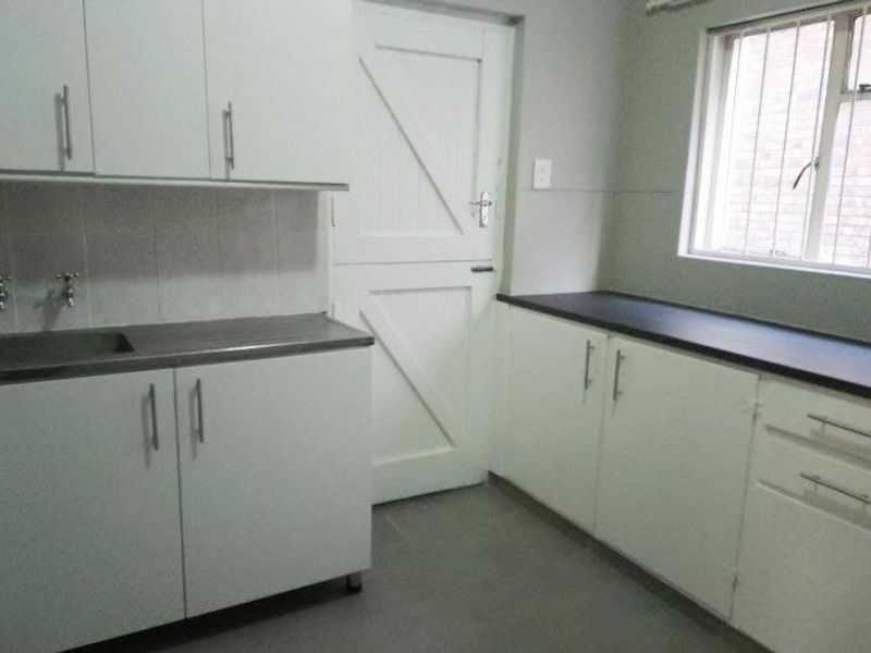 A functional scullery or laundry area featuring white built-in cabinetry, stainless steel sink, dark laminate countertops, and a stable-style exterior door.