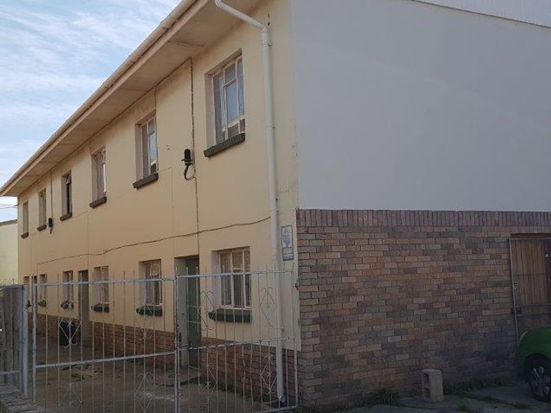 Exterior view of a multi-story apartment building featuring a brick and plastered facade, metal security gate, and a concrete driveway.