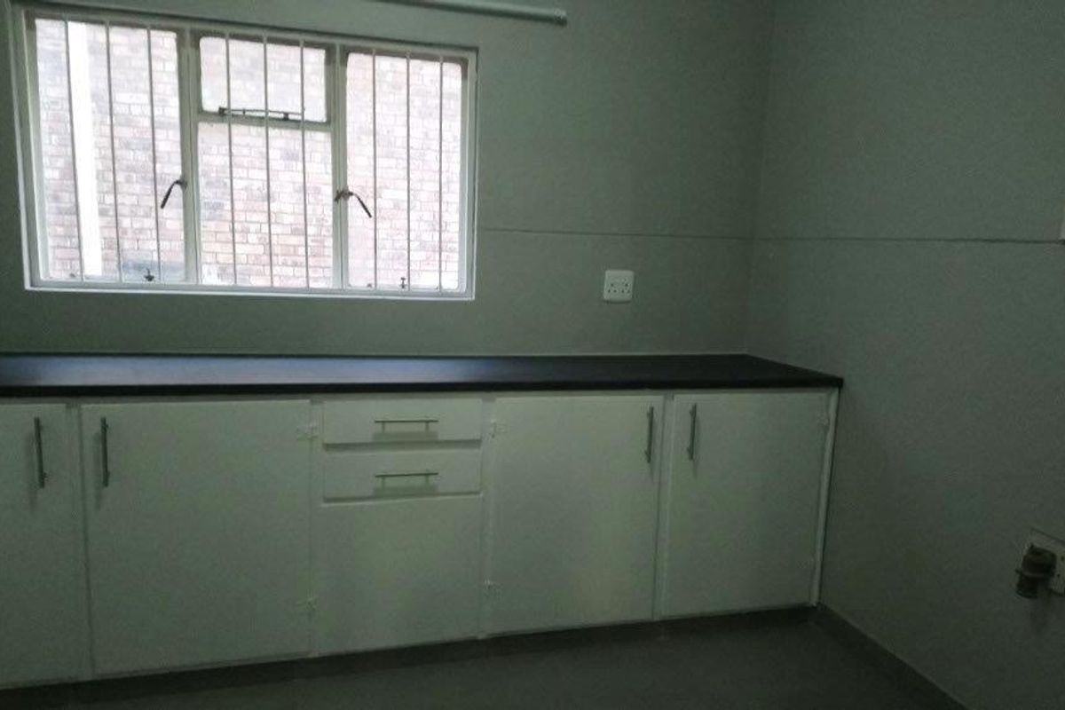 A functional kitchen area featuring white built-in cabinetry, dark laminate countertops, and a window with security bars.