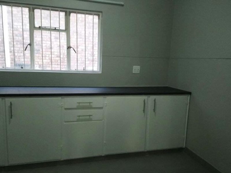 A functional kitchen area featuring white built-in cabinetry, dark laminate countertops, and a window with security bars.