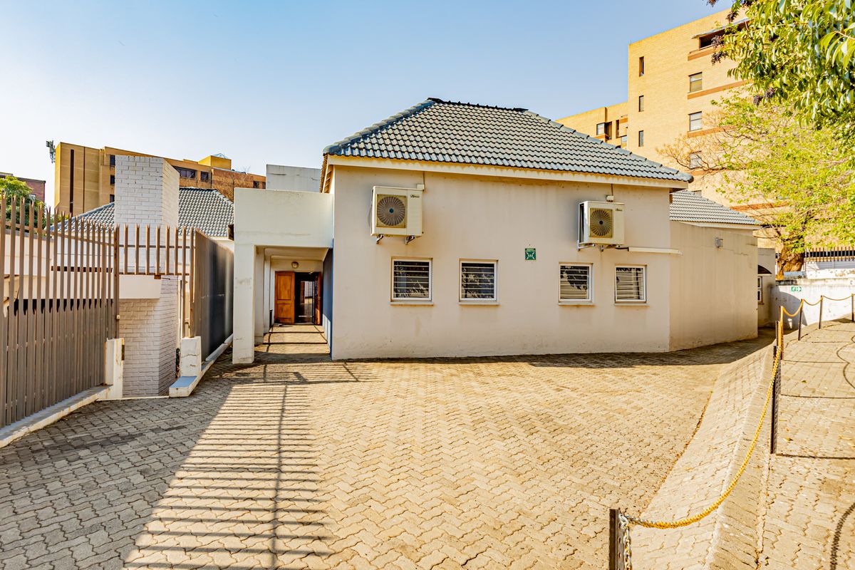 Rear exterior view of the commercial property featuring a paved driveway, security fencing, and wall-mounted air conditioning units.