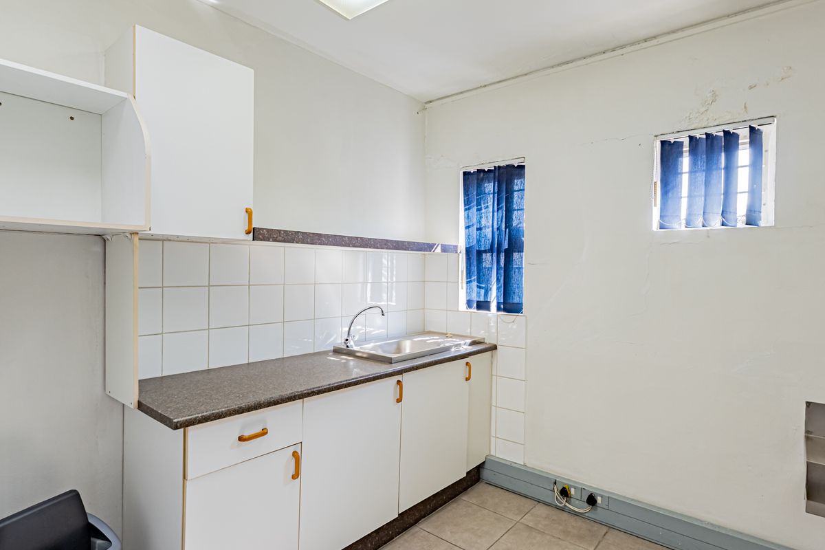 A functional kitchenette featuring laminate countertops, a stainless steel sink, tiled backsplash, and built-in cabinetry, suitable for office or utility use.