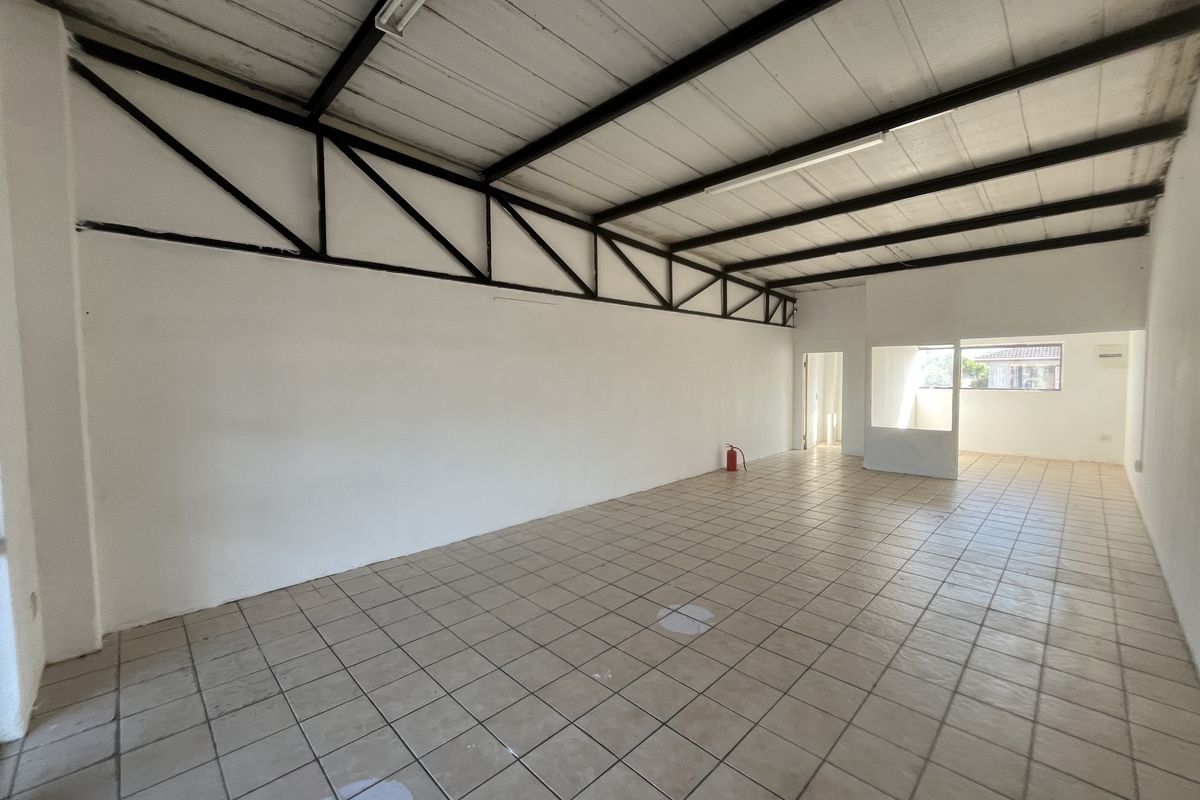An open-plan commercial space featuring tiled flooring, exposed steel roof trusses, and fluorescent lighting, suitable for various business applications.