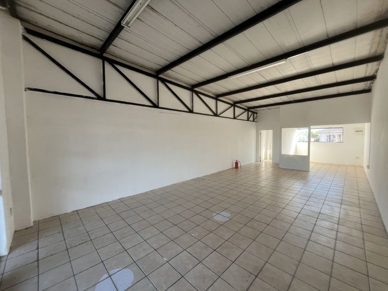 An open-plan commercial space featuring tiled flooring, exposed steel roof trusses, and fluorescent lighting, suitable for various business applications.