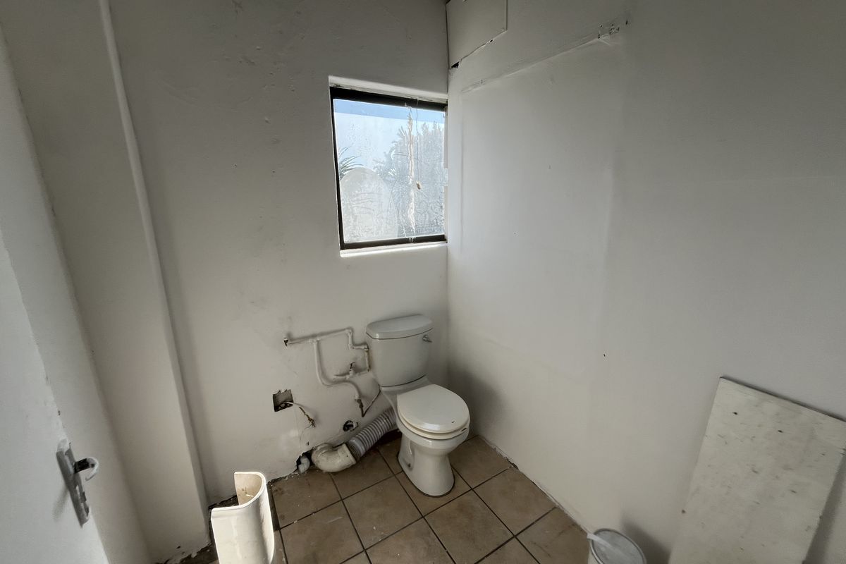 A small, unfinished bathroom space featuring a toilet, tiled flooring, and exposed plumbing, requiring renovation to restore functionality and aesthetic appeal.
