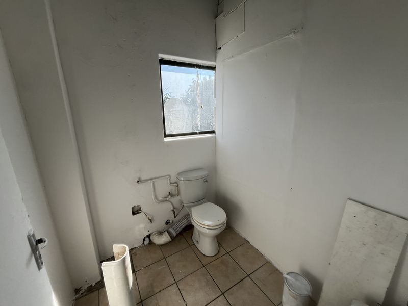 A small, unfinished bathroom space featuring a toilet, tiled flooring, and exposed plumbing, requiring renovation to restore functionality and aesthetic appeal.