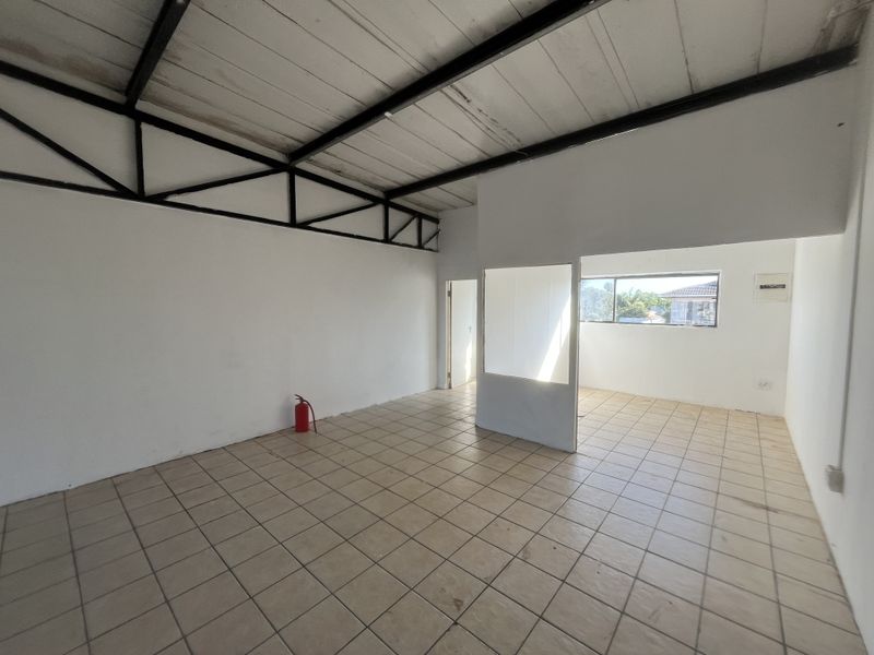 An open-plan office space featuring exposed steel roof trusses, ceramic tile flooring, and a partial partition wall, providing a functional and versatile commercial layout.