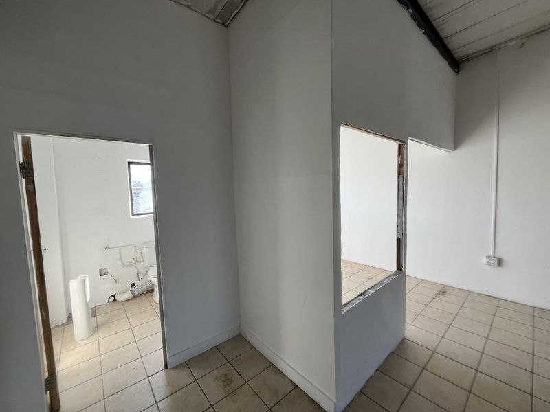 An unfinished utility or office space featuring ceramic tiled flooring, exposed ceiling beams, and internal partition walls with exposed door frames.