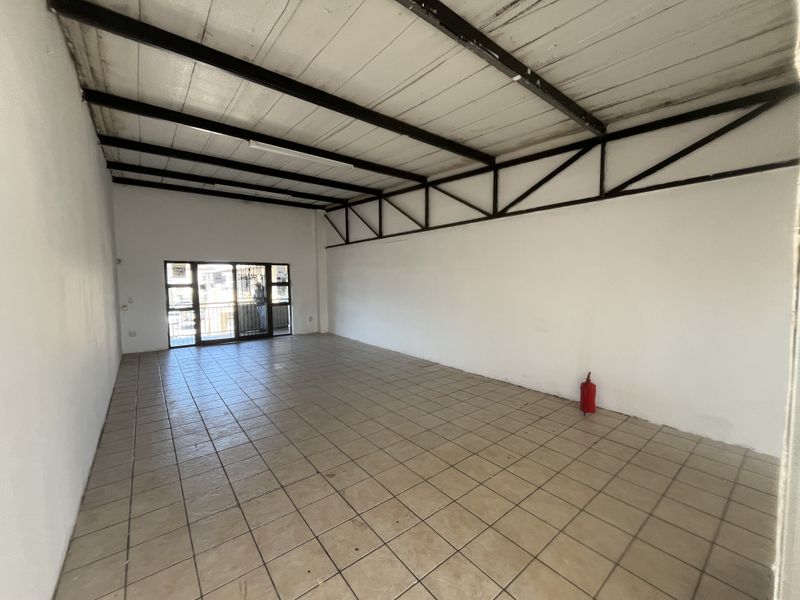 An open-plan commercial space featuring exposed steel roof trusses, tiled flooring, and a sliding glass door leading to an exterior balcony.