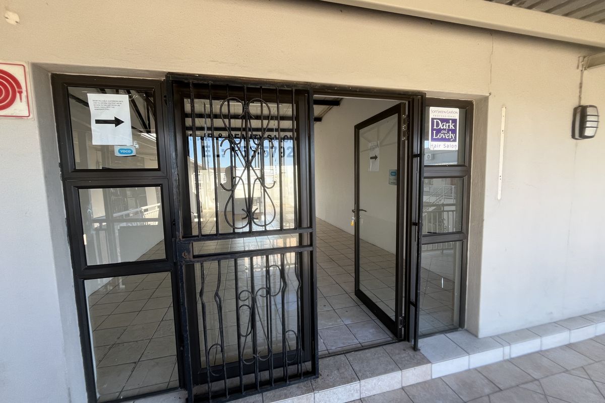 Entrance to a commercial unit featuring a security gate, aluminium-framed glass door, and tiled flooring, suitable for a salon or retail space.