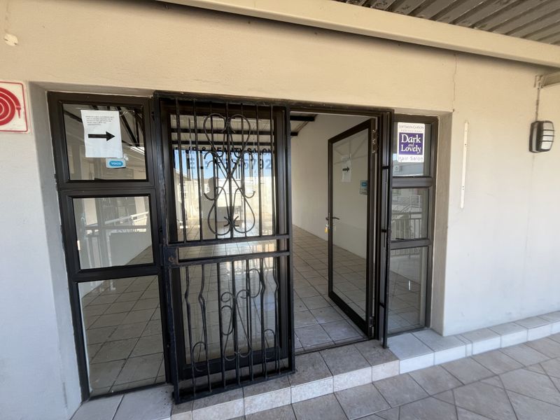 Entrance to a commercial unit featuring a security gate, aluminium-framed glass door, and tiled flooring, suitable for a salon or retail space.