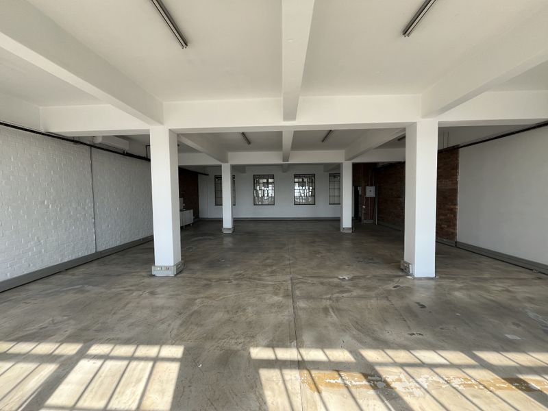 Spacious open-plan industrial commercial space featuring polished concrete floors, exposed structural columns, brick accents, and large steel-framed windows providing ample natural light.