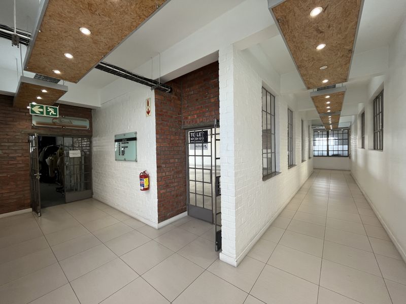 A bright, modern commercial hallway featuring industrial-style exposed brick walls, tiled flooring, and unique recessed ceiling panels with integrated lighting.
