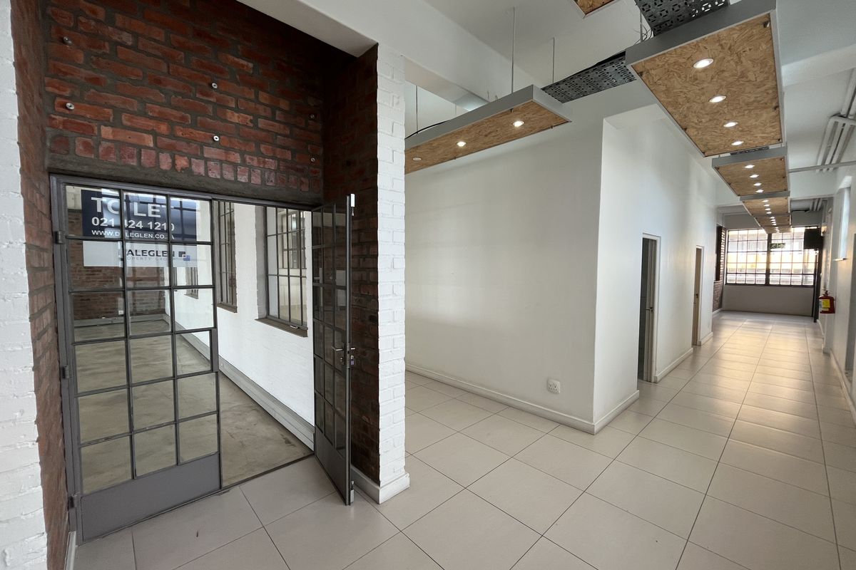 Modern industrial-style office hallway featuring exposed brickwork, tiled floors, and suspended ceiling panels with recessed lighting.